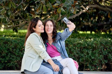 Parkta cep telefonuyla selfie çeken bir bayan arkadaş. Teknoloji ve arkadaşlık kavramı.