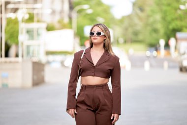 Güneş gözlüklü genç sarışın kız şehrin sokaklarında geziyor, stil ve güven saçıyor..