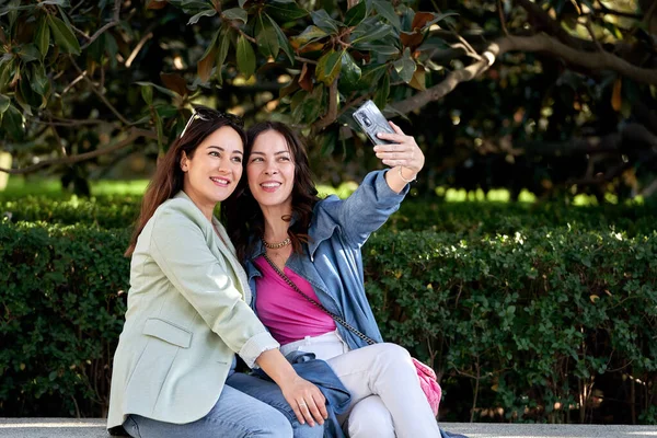 Parkta cep telefonuyla selfie çekerken gülümseyen kadın arkadaşlar. Teknoloji ve arkadaşlık kavramı.
