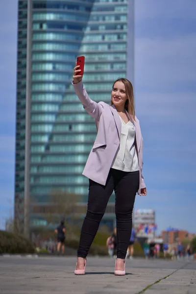 若い女性のエグゼクティブは 背景に高層ビルがある金融街の中心部で自撮りします — ストック写真