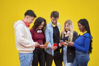 Çok ırklı arkadaşlar açık havada cep telefonlarına bakıyorlar. Teknoloji ve arkadaşlık kavramı.
