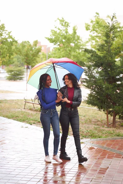 在一个多彩的雨天 两个女人 非洲裔美国人和拉美人 在公园里散步 — 图库照片