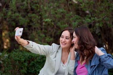 Parkta cep telefonuyla selfie çeken bir bayan arkadaş. Teknoloji ve arkadaşlık kavramı.