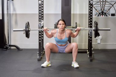 Güçlü ve kararlı genç bir kadın yoğun idmanı sırasında ağır bir halterle omuz presi yapıyor.. 