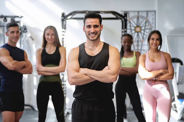 Spor salonunda kollarını kavuşturup kameraya poz veren bir grup fitness ve çok ırklı insan.