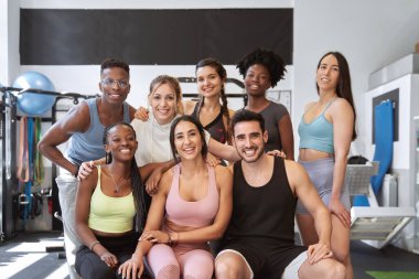 Çok kültürlü fitness grupları kameraya bakıyor ve spor salonunda gülümsüyor.