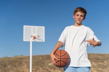 Genç bir çocuk dışarıda, spor sahasında basketbol topuyla poz veriyor. Spor konsepti.