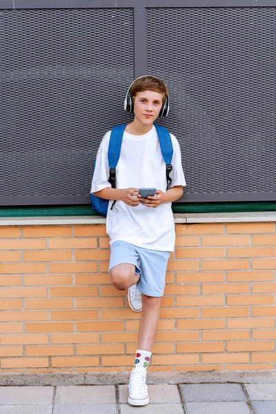 Ung Pojke Med Hörlurar Tittar Kameran Medan Håller Mobiltelefon Stående — Stockfoto