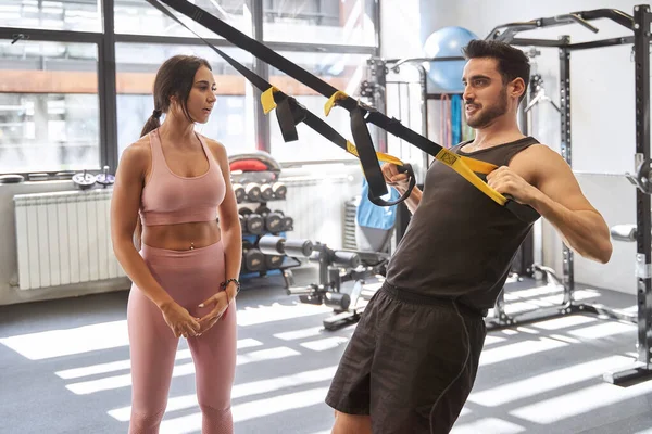 Spor salonunda spor salonundaki özel bayan antrenörüyle süspansiyon kayışlarıyla egzersiz yapıyor. Spor konsepti.