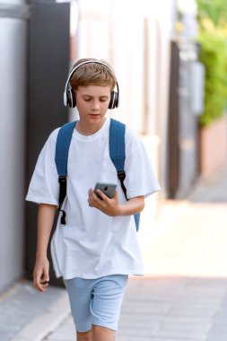 Genç çocuk sokakta yürürken cep telefonu ve kulaklık kullanıyor. Teknoloji konsepti.