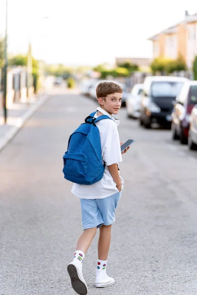 Teenage student with backpack walking down the street with mobile phone and headphones.