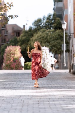 Elinde vantilatörle sokakta yürürken gülümseyen bir kadın. Yaz konsepti.