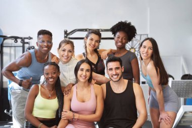 Çok kültürlü fitness grupları kameraya bakıyor ve spor salonunda gülümsüyor.