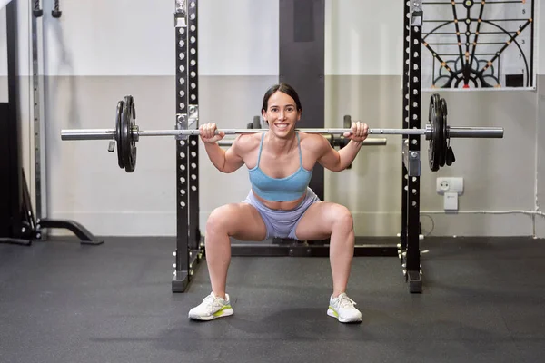 A powerful and determined young woman performing a shoulder press with a heavy barbell during her intense workout session.