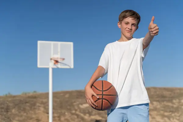 Mladý Chlapec Ukazuje Palec Nahoru Zatímco Pózuje Basketbalovým Míčem Venkovním — Stock fotografie