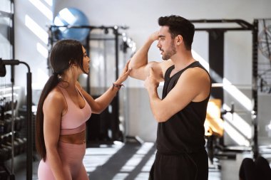Fitness adamı, spor salonunda kadın ortağına kol kaslarını gösteriyor. Spor konsepti.