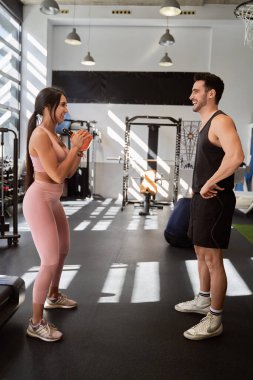 Spor salonunda kişisel antrenörle antrenman yaparken spor salonundaki kadın kettlebell ile egzersiz yapıyor. Spor konsepti.