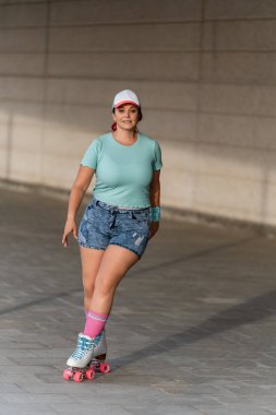  Güneşli bir günde, yaz kıyafetleri ve şapkalı patenci kadın sokakta paten kayıyor..