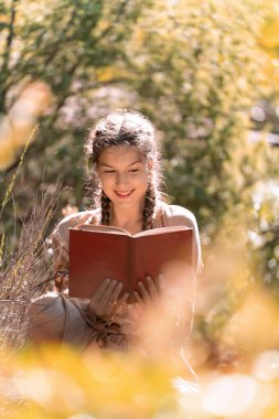 Güneşli bir günde, sonbahar ormanının ortasında oturmuş kitap okuyan güzel genç bir kadın..