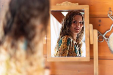 Evde aynada kendine bakarken gülümseyen genç bir kadın..