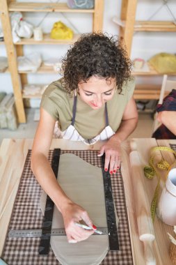 Çömlek atölyesinde çalışırken kilden bir parça kesen ve ölçen bir kadın. Hobi ve el işi konsepti.
