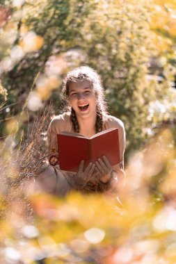 Güneşli bir günde açık havada kitap okurken gülümseyen mutlu genç adam..