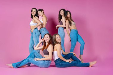 Kot pantolonlu ve beyaz tişörtlü altı oyuncu kadın pembe stüdyo geçmişine karşı eğlenceli bir anın tadını çıkarıyorlar..