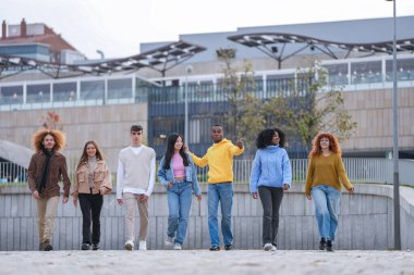 Şehir manzarasında ilerleyen altı arkadaş grubu, modern mimariyle birlik ve güven gösteriyorlar..