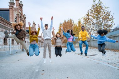 Bir grup arkadaş birlikte sıçrıyor, heyecan dolu, tarihsel bir ara sokakta, gençliğin canlı bir sembolü olan sonbahar ağaçlarıyla dolu.