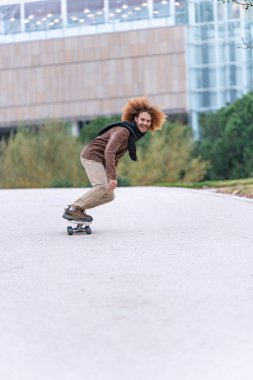 Coşkulu kaykaycı, şehir yeşilliği ve modern binalarla dolu bir yolda bir numara yapıyor..