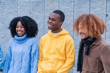 Neşeli üçlü, neşeli bir anı paylaşıyor kahkahaları, basit bir gri duvarın arka planında yankılanıyor.