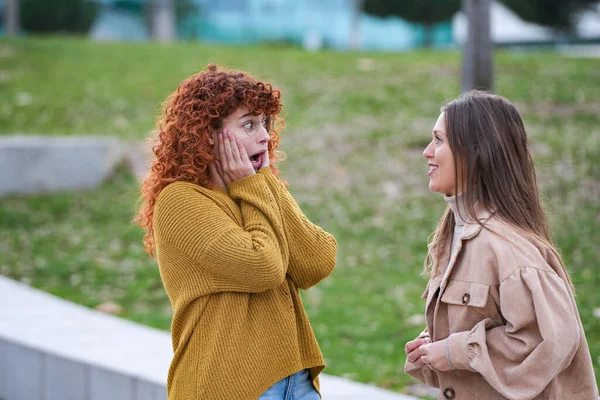 Woman looking surprised at her friend while talking together outdoors. Friendship concept.