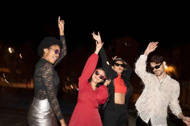 Geceleri neşeyle dans eden dört arkadaş, arkada sokak lambaları. 