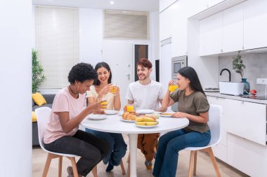 Çeşitli etnik kökenlerden dostların kahvaltı sırasında kahkahalarını paylaştığı samimi bir sahne.