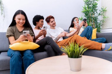 Çeşitli arkadaşlar kanepede gülümsüyor ve akıllı telefonlar kullanıyor. Teknolojik etkileşimden keyif alıyorlar.. 