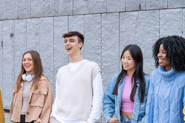 Genç bir arkadaş grubu, dokulu bir duvarın önünde gerçek gülücükler ve kahkahalarla eğleniyor.