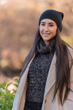 Bereli ve ceketli neşeli genç bir kadın güneşli bir sonbahar öğleden sonrasının tadını çıkarıyor.. 