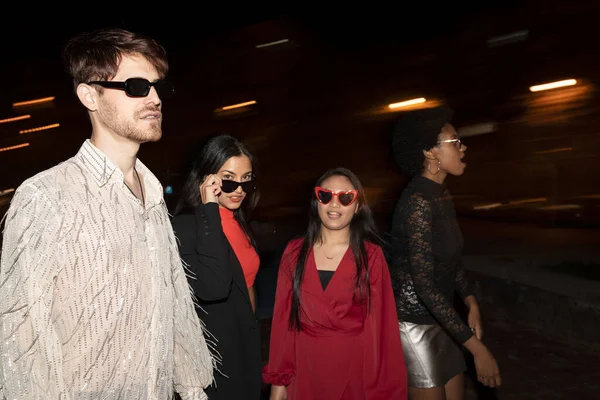Four stylish friends make a bold statement with their evening wear and sunglasses, walking confidently at night