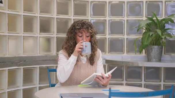 Krullenbol Vrouw Nippen Koffie Het Lezen Van Een Notitieboekje Aan — Stockvideo