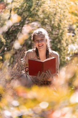 Güneşli bir günde açık havada kitap okurken gülümseyen mutlu genç adam..