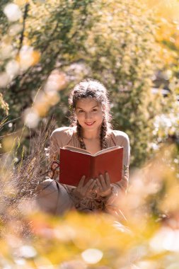 Doğada kitap okurken gülümseyen genç bir kadın..