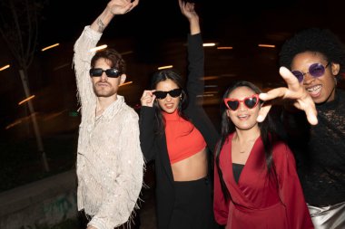 Heyecanlı arkadaşlar bir gecede dans ediyorlar, benzersiz güneş gözlükleriyle şahsi tarzlarını sergiliyorlar, şehir ışıkları altında.