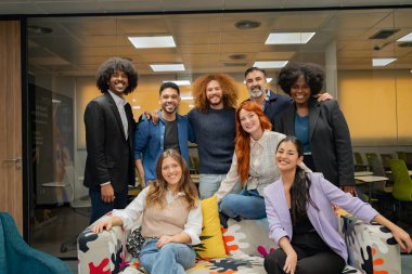 Modern bir ofis salonunda gülümseyen ve poz veren çeşitli profesyonellerden oluşan bir grup takım ruhu ve işbirliği gösteriyor.. 