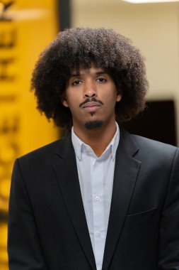 Takım elbiseli, afro saçlı profesyonel bir adam ciddi bir şirket ortamında duruyor.. 