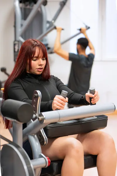 Focused Woman Black Sportswear Using Leg Press Machine Busy Gym lizenzfreie Stockbilder