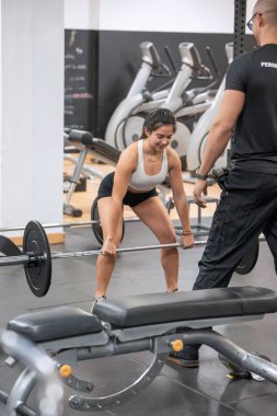 Genç bir kadın, iyi donanımlı bir spor salonunda kişisel antrenörünün rehberliğinde kaldırma egzersizi yapıyor.. 