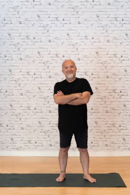 60 yaşında yoga kıyafeti giymiş, kolları hasırda duran bir adam.. 