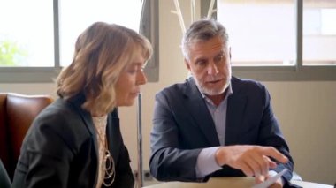 Çağdaş bir ofis ortamında, iki profesyonel çeşitli belgeleri incelemeye odaklanıyor