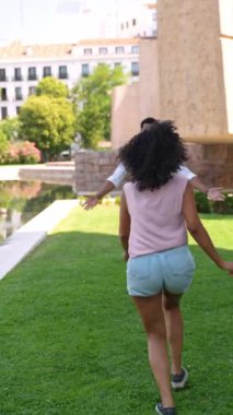 Bir adam, yeşil çimenler ve arka plandaki büyük binalarla çevrili, neşeli bir parkta bir kadını kaldırır ve döndürür. Güneşli günün tadını çıkarır.. 