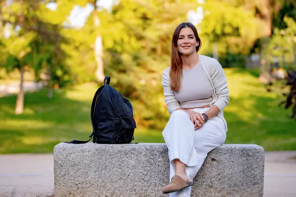 Parktaki bankta huzur içinde dinlenen genç bir kadın. Rahatlamış ve memnun. Etrafı huzur ve özgürlükle çevrili.